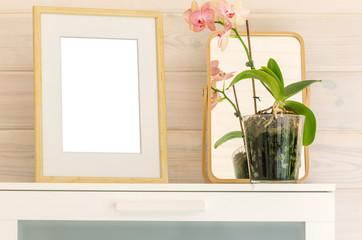 Wooden frame mock up and phalaenopsis orchid on a white chest in a bedroom of a wooden house with white trim.