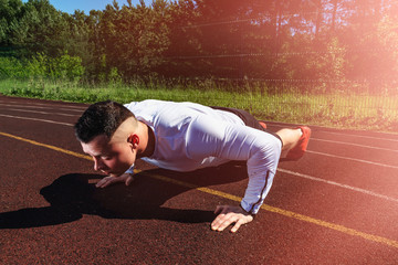 Young man in sportswear making pushups on a stadium