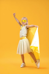 Cute little girl dressed as superhero on color background