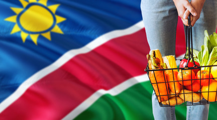 Woman is holding supermarket basket, Namibia waving flag background. Economy concept for fresh fruits and vegetables.