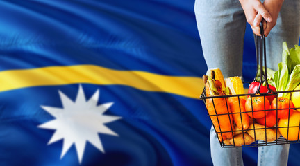 Woman is holding supermarket basket, Nauru waving flag background. Economy concept for fresh fruits and vegetables.