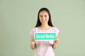 Fototapeta na wymiar Female Asian blogger holding paper with text SOCIAL MEDIA on color background