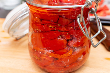Homemade dried red  tomatoes slices with basil oregano spices in a glass jar. Traditional Italian Mediterranean kitchen cuisine.