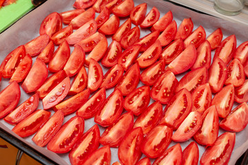 Homemade dried red  tomatoes slices with basil oregano spices cooking process. Traditional Italian Mediterranean kitchen cuisine.