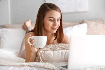 Beautiful young woman with laptop drinking tea at home