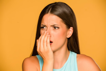 Portrait of beautiful young woman checking her breath on yellow background