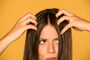 Beautiful young woman with itchy scalp on yellow background