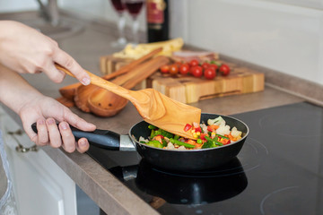Girl cooks vegetables on the stove, stirring with a wooden shovel.