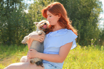 Cheerful pretty young woman sitting and hugging her dog on the nature