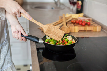 Girl cooks vegetables on the stove, stirring with a wooden shovel.