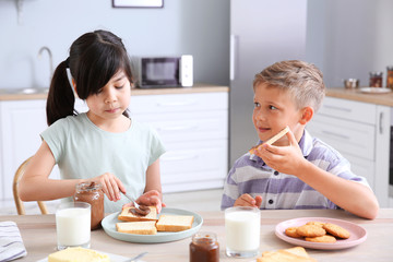 Obraz na płótnie Canvas Funny little children eating tasty toasts in kitchen