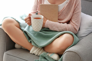 Fototapeta premium Young woman with book drinking hot tea at home