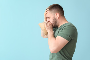 Man with paper bag having panic attack on color background