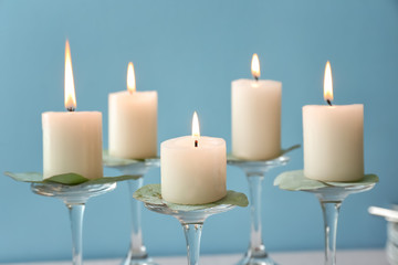 Glass stands with beautiful burning candles on color background