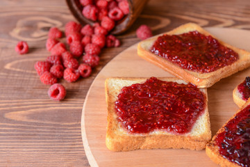 Tasty toasted bread and raspberry jam on wooden board