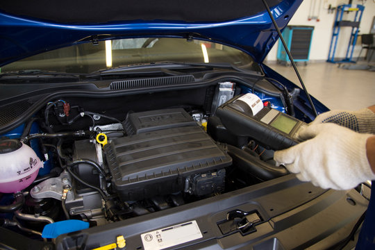 A professional car mechanic works in a car service. Mechanic service using Multimeter to check the voltage level in a car battery Car diagnostics.