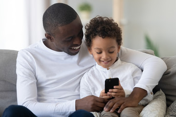 Happy black dad teaching kid son holding phone using apps