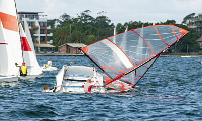 Children climbing back into a capsized sailboat with on an inlan
