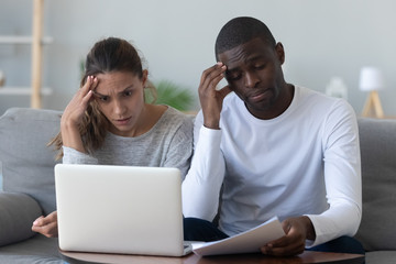 Shocked worried young mixed race family couple calculate bills