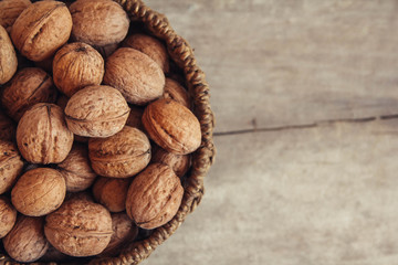 Walnuts in a round wicker basket on a wooden background. Top view. Copy, empty space for text