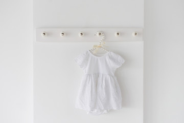 A newborn white dress on a hanger in a  light room. Waiting a baby concept.
