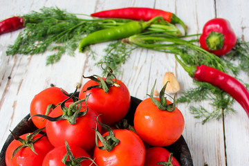 Fresh organic red tomatoes in black plate on white wooden table with green and red and chilli peppers,green peppers,black peppercorns,salt,close up,healthy concept