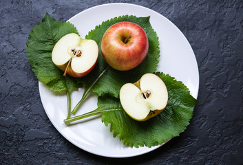 An apple with green leaves lying on the white plate. Still life photo. Black background. Fruit and nature.