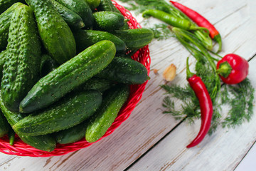 Fresh organic cucumbers in red basket  on white wooden table with green and red and chilli peppers,fennel,salt,black peppercorns,garlic,pea,close up,healthy concept,top view,flat lay