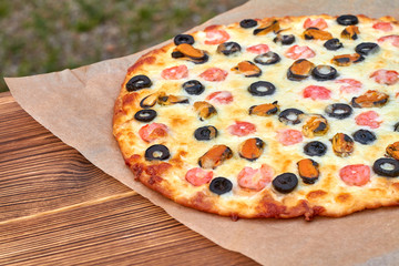Delicious homemade pizza with seafood on parchment and wooden board. Cooking homemade pizza with shrimp, mussels, black olives and mozzarella. Closeup, selective focus
