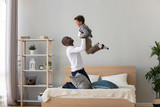 Happy black father holding lifting child son playing on bed