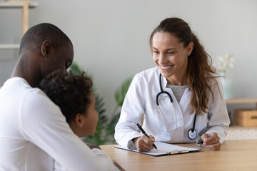Smiling female doctor listen cute african boy make notes