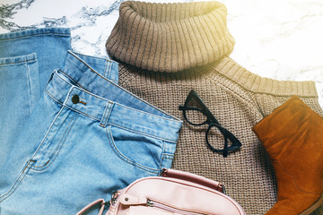 Woman clothes and accessories set on marble background.Women's warm sweater, jeans,camel boots, pink bag.Modern and casual outfit.Shopping concept. Fashion blog or magazine concept.Flat lay, top view