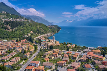 Naklejka na ściany i meble The resort town of Pulciano, located on the shores of Lake Garda. San Michele Arcangelo Church is located on a mountain. Panoramic view of the city, church, Lake Garda, Alps. Aerial view.