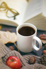 Autumn, fall leaves, hot steaming cup of coffee and a warm scarf or cardigan on black old background. Seasonal, morning coffee, Sunday relaxing and still life concept.Space for copy