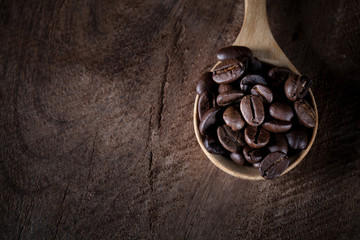 coffee beans on wooden spoon on the brown wood table.