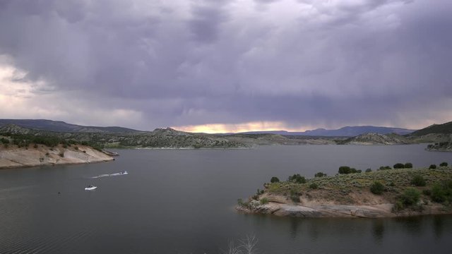 View of 2 boats on Red Fleet Reservoir with storm clouds overhead as they waterski.