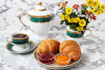 French breakfast with croissants,apricot jam,cherry jam and a cup of tea,red and yellow flowers on white concrete background,close up,space for text,Valentine`s Day breakfast