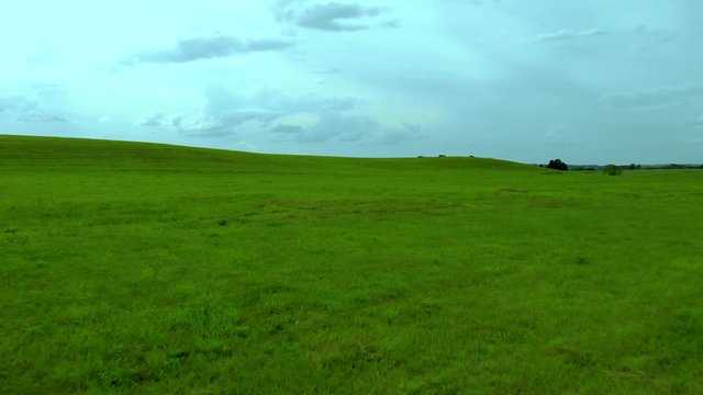 Slow fly over green grass field, blue sky and grey clouds, aerial shot, cinema look