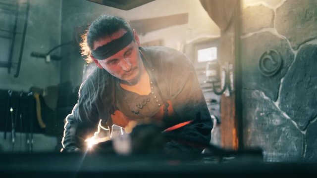 Forge worker heats metal knife, holding it with tongs.