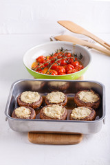 Baked stuffed champignon caps and baked cherry tomatoes on white table. Mushrooms stuffed with vegan cashew mayonnaise on baking sheet. Vegetarian food concept.