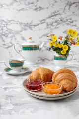 French breakfast with croissants,apricot jam,cherry jam and a cup of tea,red and yellow flowers on white concrete background,close up,space for text,Valentine`s Day breakfast