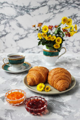 French breakfast with croissants,apricot jam,cherry jam and a cup of tea,red and yellow flowers on white concrete background,close up,space for text,Valentine`s Day breakfast