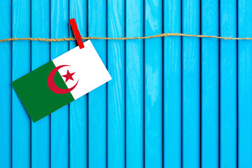 Flag of Algeria hanging on clothesline attached with wooden clothespins on aqua blue wooden...