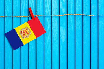 Flag of Andorra hanging on clothesline attached with wooden clothespins on aqua blue wooden background. National day concept.