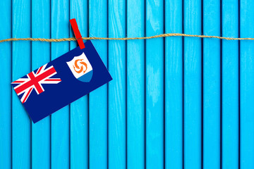 Flag of Anguilla hanging on clothesline attached with wooden clothespins on aqua blue wooden background. National day concept.