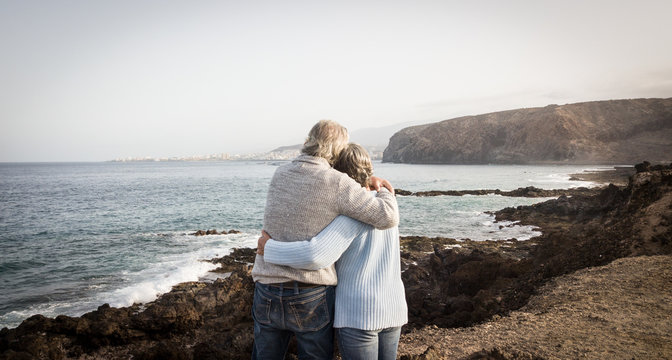 Love forever for two senior people standing on the cliff of the ocean. Morning soon outdoor with clear sky. Vacation and happiness for pensioners - Powered by Adobe