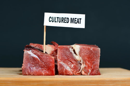 Big Raw Red Meat Chunks On Wooden Plate With Label Saying 'cultured Meat', Concept For Artificial Meat Production