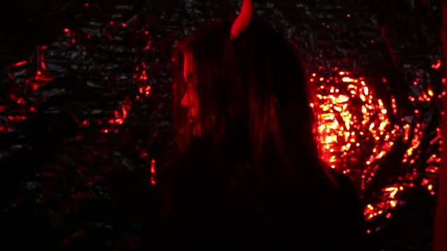 Girl in the form of a devil with horns. Image of halloween in red light. Contact lenses and a scary look.