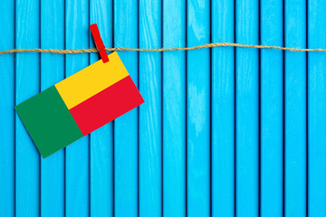Flag of Benin hanging on clothesline attached with wooden clothespins on aqua blue wooden background. National day concept.