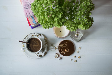 A cup of coffee with female accessories and hydrangea flower on a table, top view.